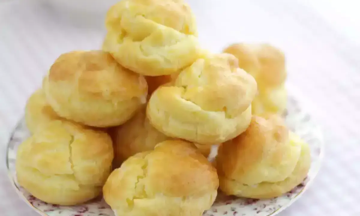 En hög med gyllene petit choux på en vacker tallrik, redo att fyllas med grädde eller glass.