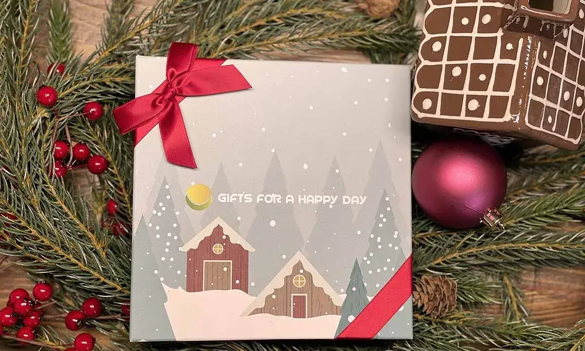 En julklapp med ett vinterlandskap och texten "GIFTS FOR A HAPPY DAY", omgiven av granris och röda bär.