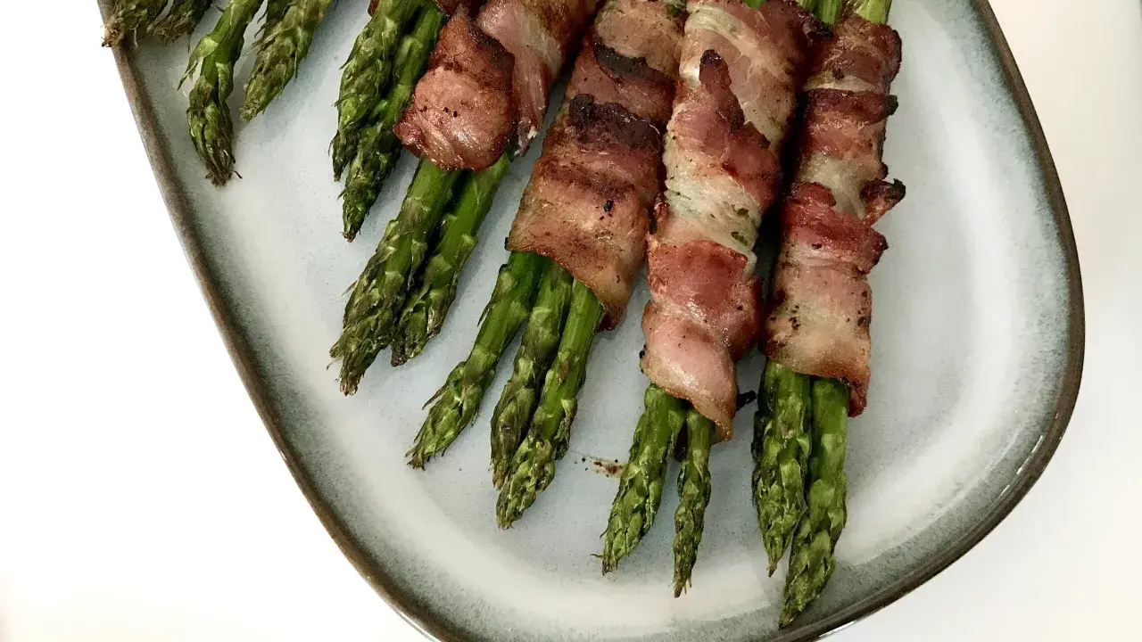 Grön sparris insvept i knaprigt bacon, serverad på en ljusblå tallrik. En läcker och enkel rätt som passar till det mesta.