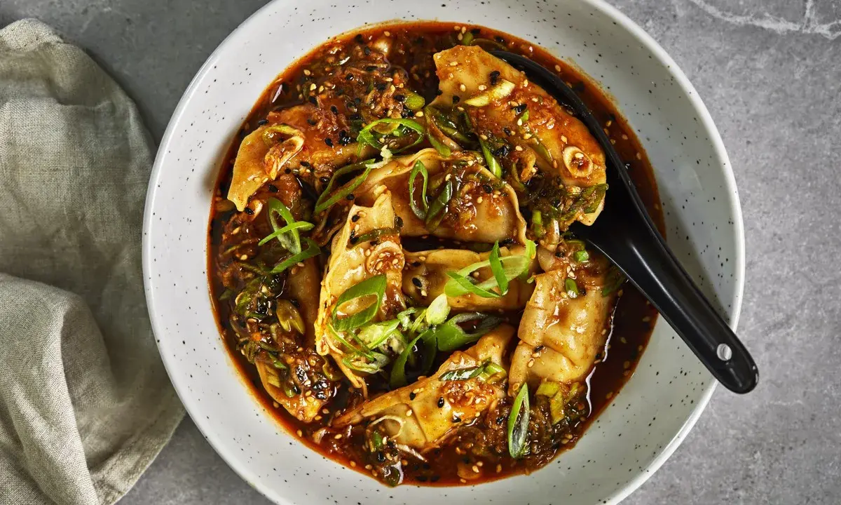 En skål med dumplings i en kryddig sås, toppad med salladslök och sesamfrön. Ett perfekt recept middag för en smakrik kväll.