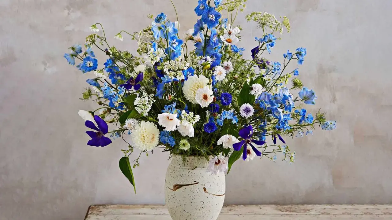 En vacker bukett med blå och vita perenna snittblommor, som riddarsporre och prästkrage, i en rustik vas.