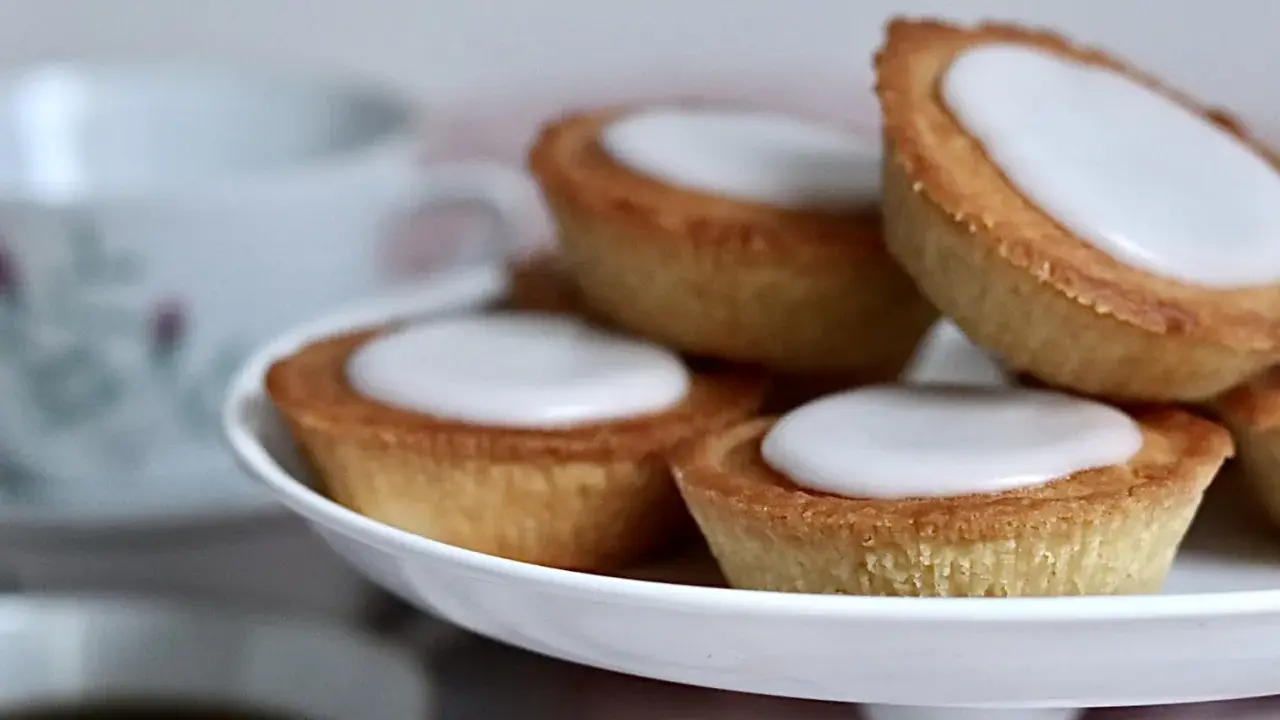 Små, gyllene mazariner med vit glasyr på ett fat. Perfekt för fikastunden, här är ett enkelt mazariner recept.