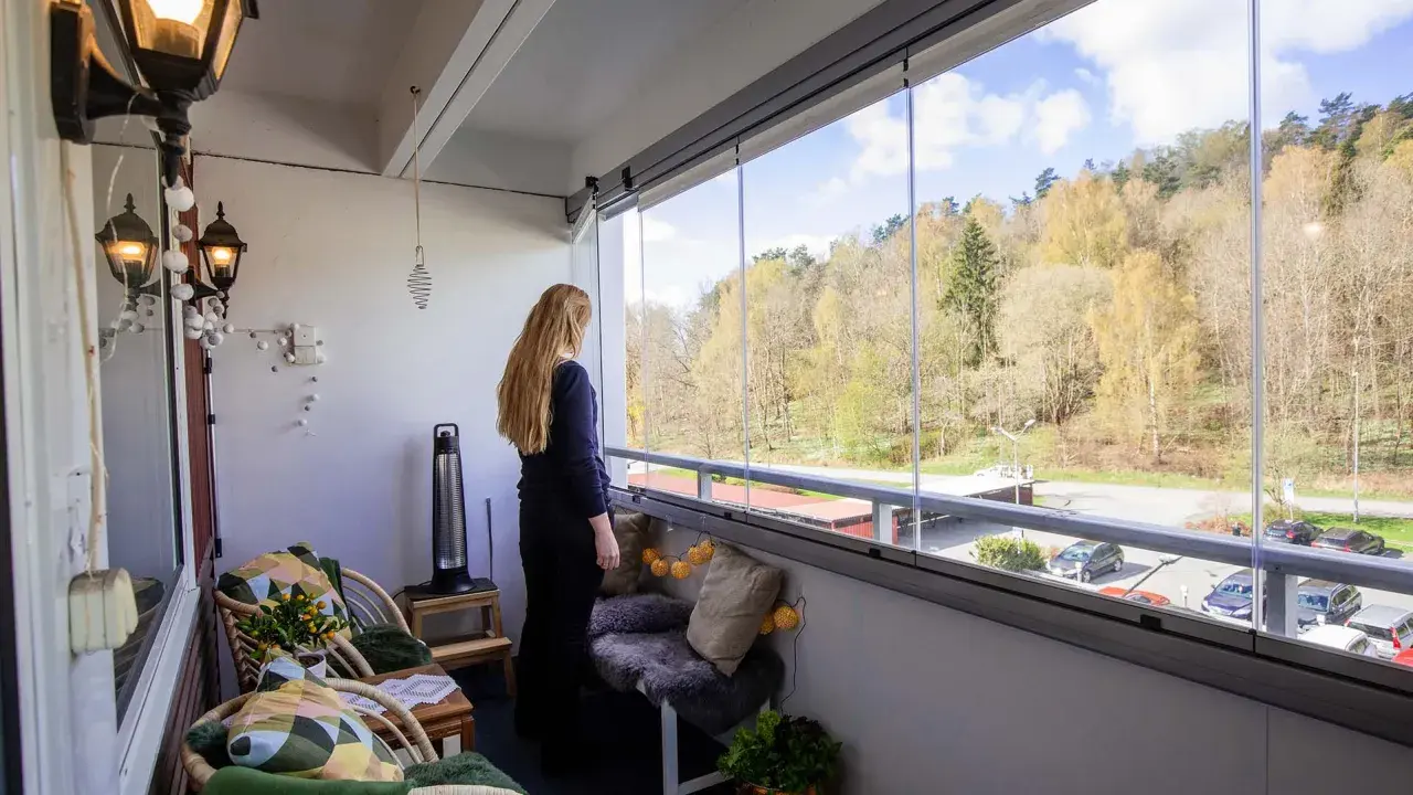 Kvinna njuter av utsikten från inglasad balkong. Mysiga sittplatser och lampor ger fina balkong tips för en ombonad känsla.