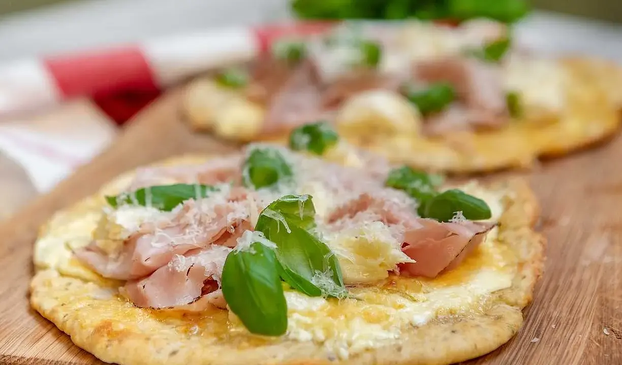 Två små pizzor med skinka, ost och basilika på en snabb pizzadeg. Serveras på en träskärbräda.