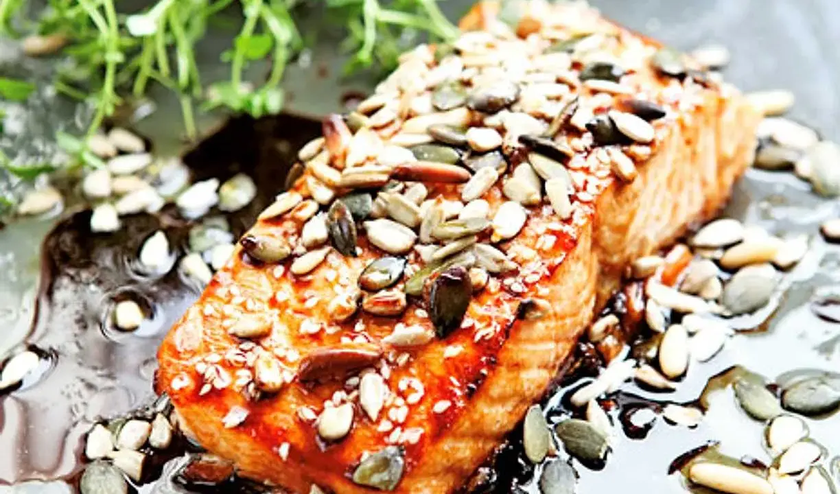 En saftig bit teriyaki lax toppad med frön, serverad i en glansig sås med gröna örter.