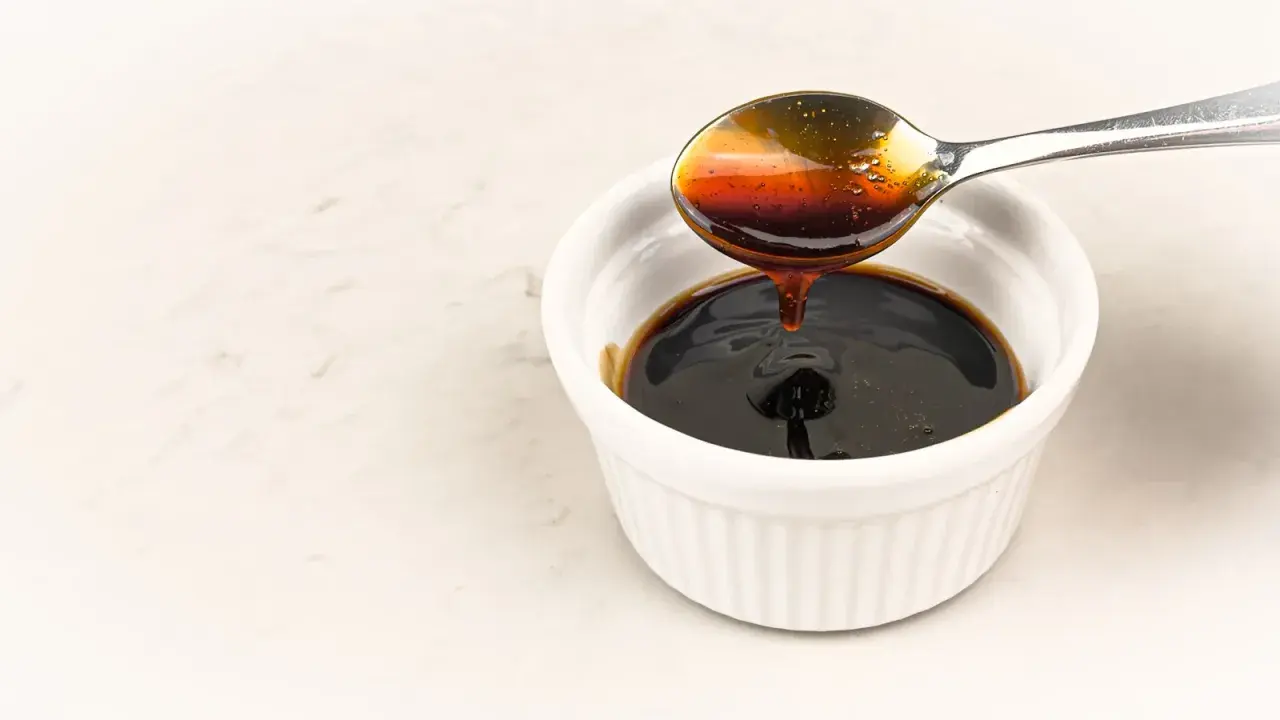 En sked häller mörk, glansig teriyakisås i en vit skål. Perfekt för ditt teriyakisås recept.