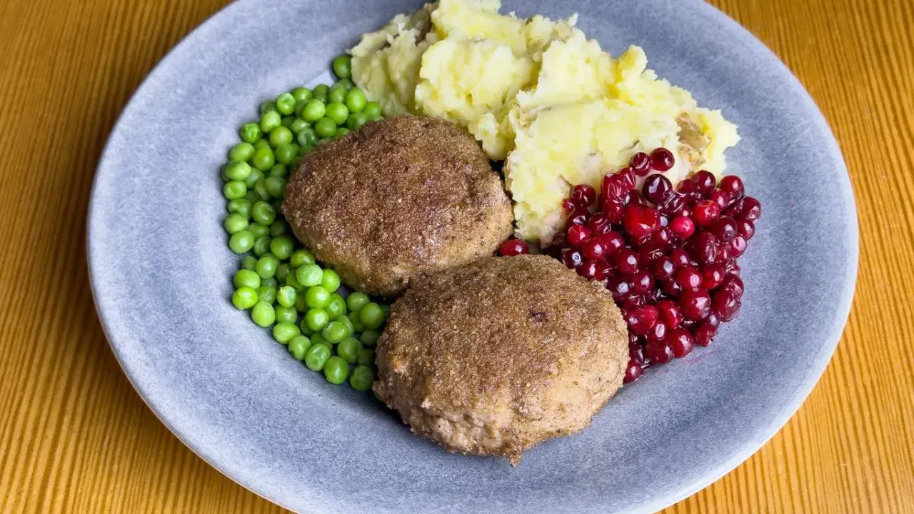 Två köttbullar med potatismos, gröna ärtor och rårörda lingon. En klassisk tallrik med svensk husmanskost.