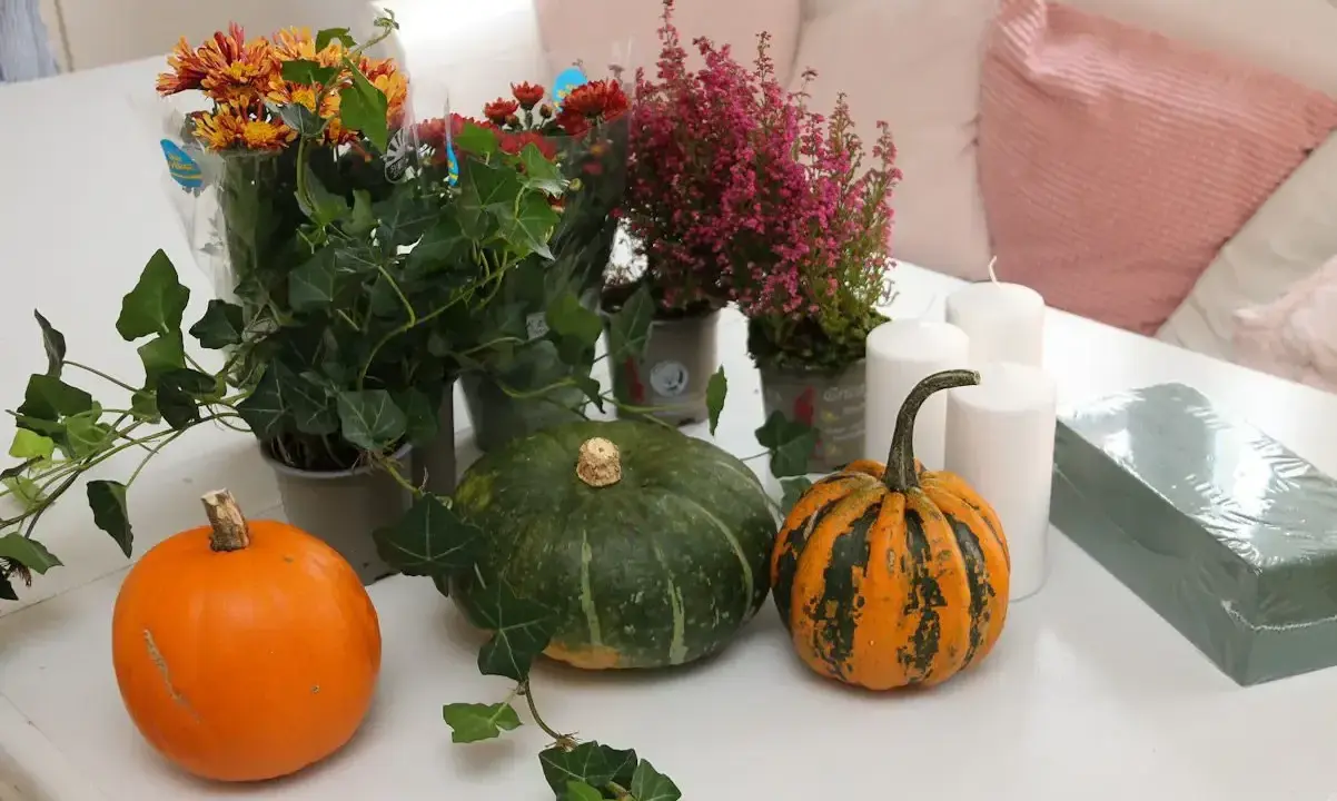 Förberedelser för att dekorera pumpa med höstblommor, ljus och murgröna.