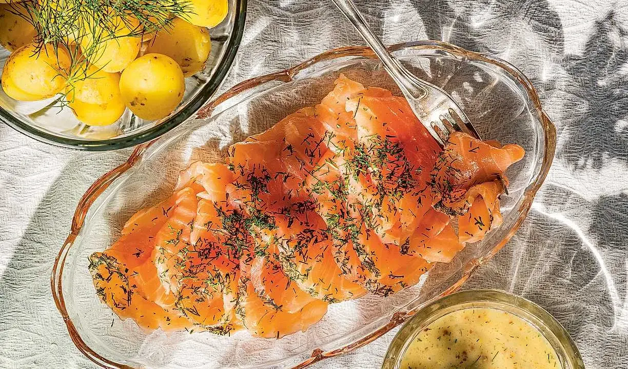 Gravlaxsås recept: Skivad gravad lax med dill, serverad med kokt färskpotatis och en skål med gravlaxsås.