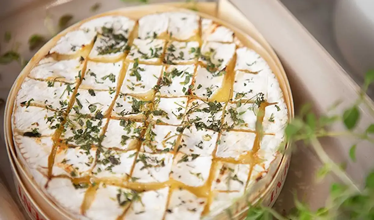 En härlig brie i ugn, gyllene och bubblande, toppad med örter. Perfekt för att doppa bröd i.