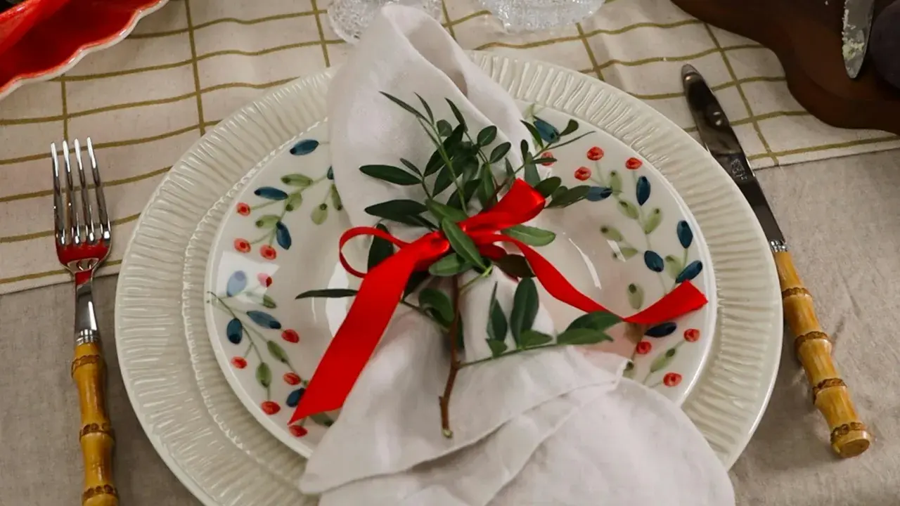 Vacker juldukning dekoration med en tallrik med bär, en vit servett med grönt och rött band, samt bestick med bambuhandtag.