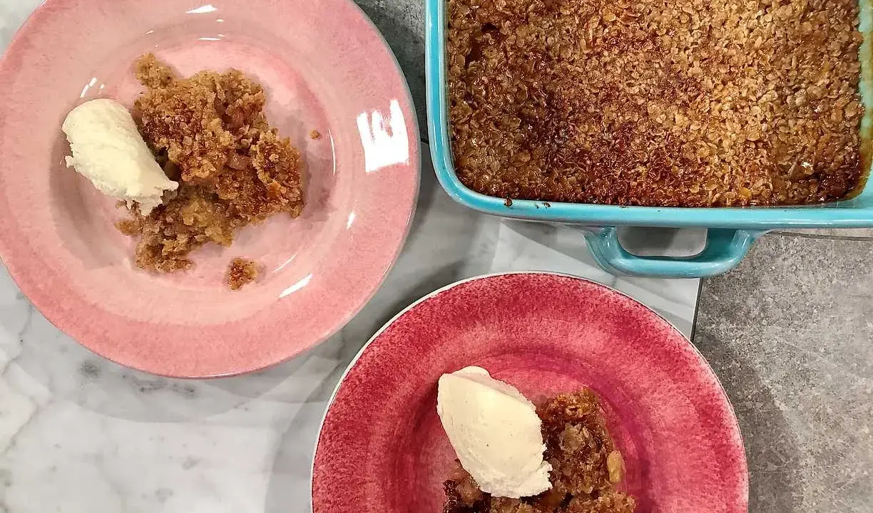En härlig glutenfri rabarberpaj med en krispig topping, serverad med vaniljglass på rosa och röda tallrikar.