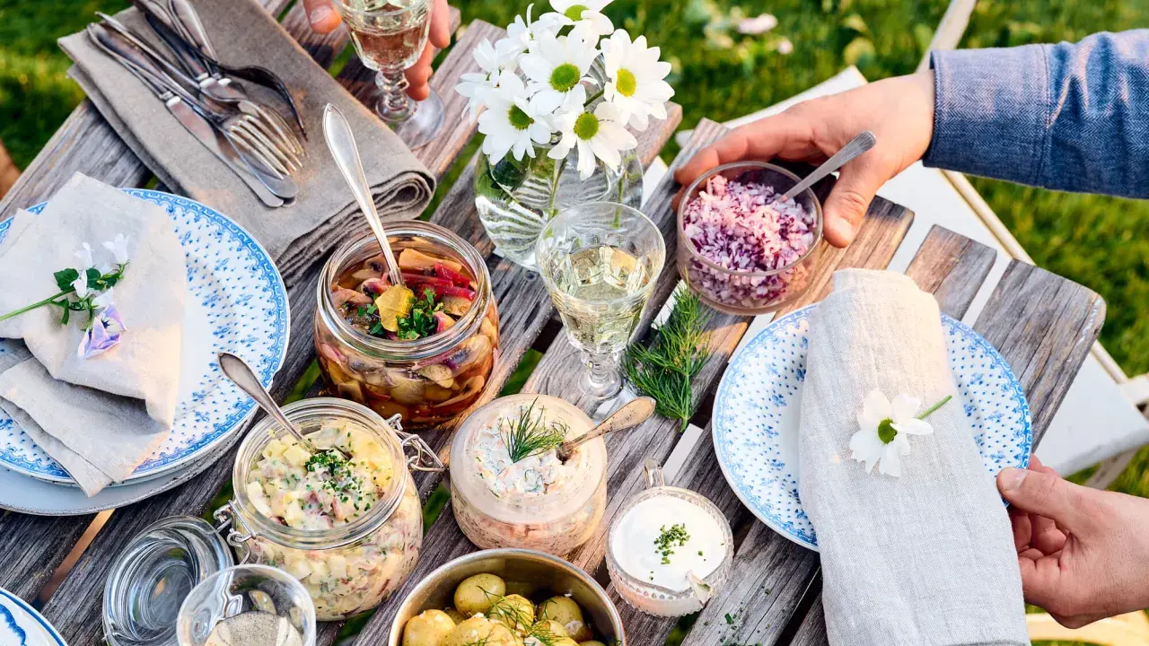 En härlig dukning med vegetarisk midsommarmat: potatissallad, sillinläggningar, gräddfil och hackad rödlök. Blommor och grönska skapar en festlig stämning.