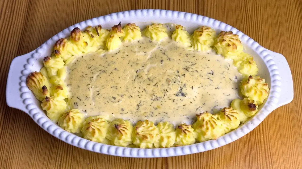 En gratinerad fiskrätt med alaska pollock recept, omgiven av spritsad potatis.