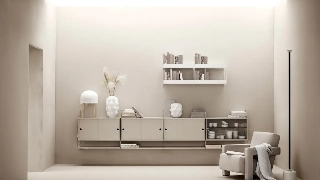 Minimalist livingrum med stringhylla inspiration. En beige fåtölj med pläd, lampa, vas och böcker på hyllor.