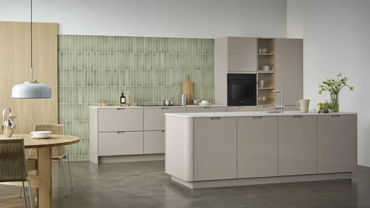 Ett modernt, hållbart kök med beige skåp, grön mosaik och ett runt matbord i trä.