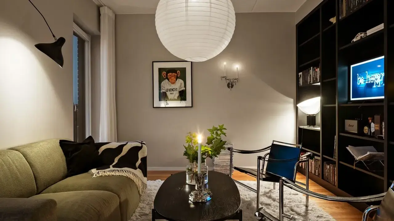 Mysig vardagsrumsmiljö med en stor papperslampa i taket. Belysning bakom gardin skapar en mjuk atmosfär.