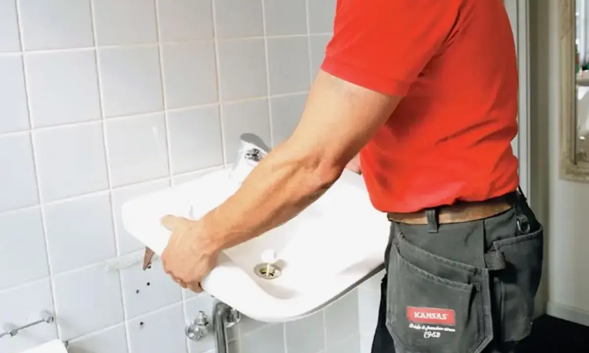 En person i röd tröja och arbetsbyxor håller i ett nytt handfat för att byta ut det gamla.