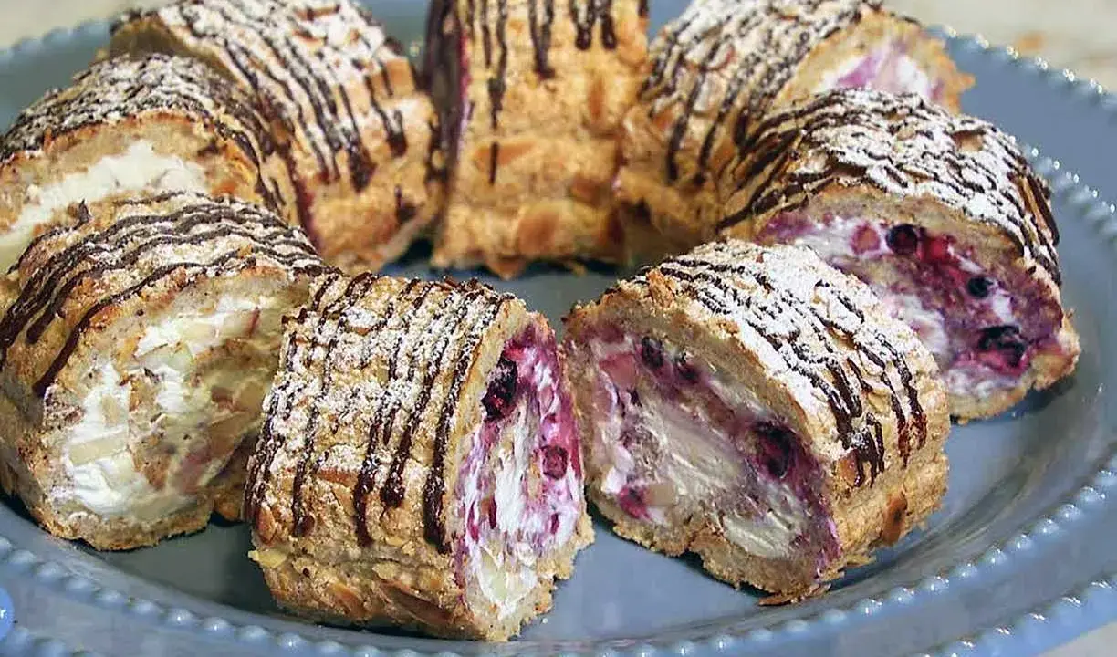 Budapestrulle recept: Skivade rulltårtor med grädde, bär och mandel, toppade med florsocker och chokladdrizzle.