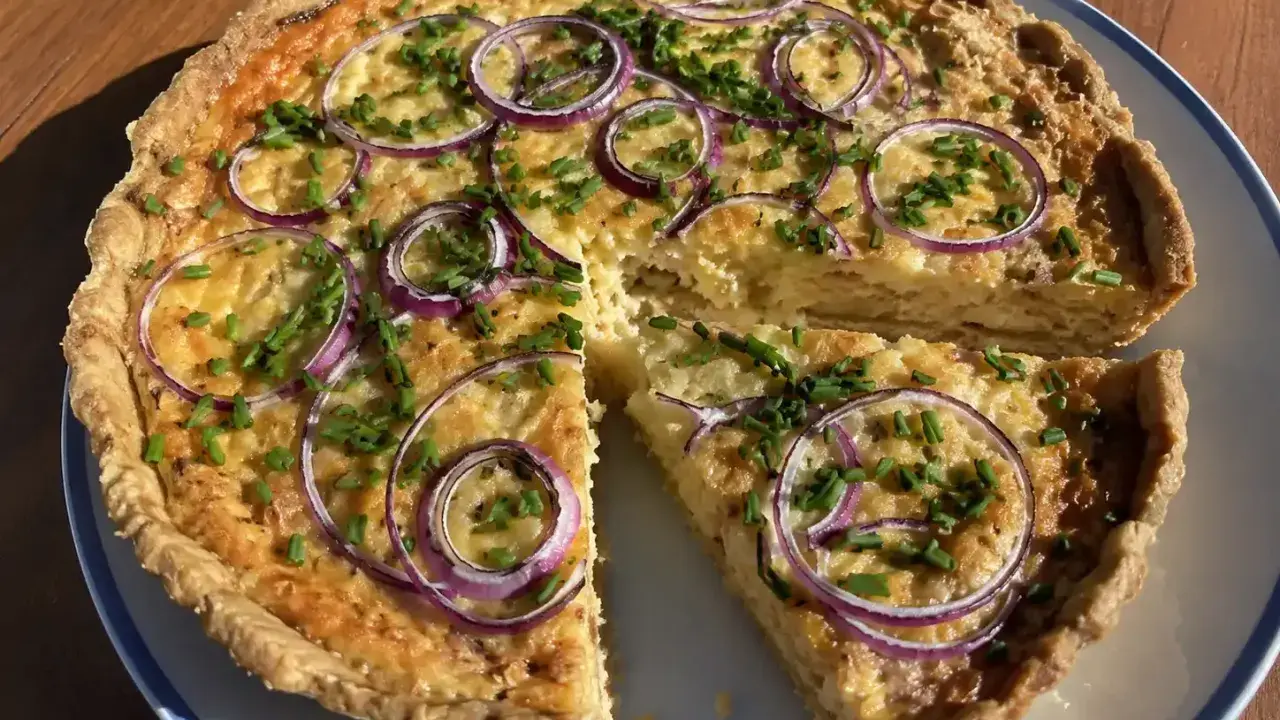 En gyllene ostpaj med rödlök och gräslök, perfekt för ett ostpaj recept. En bit är uppskuren.