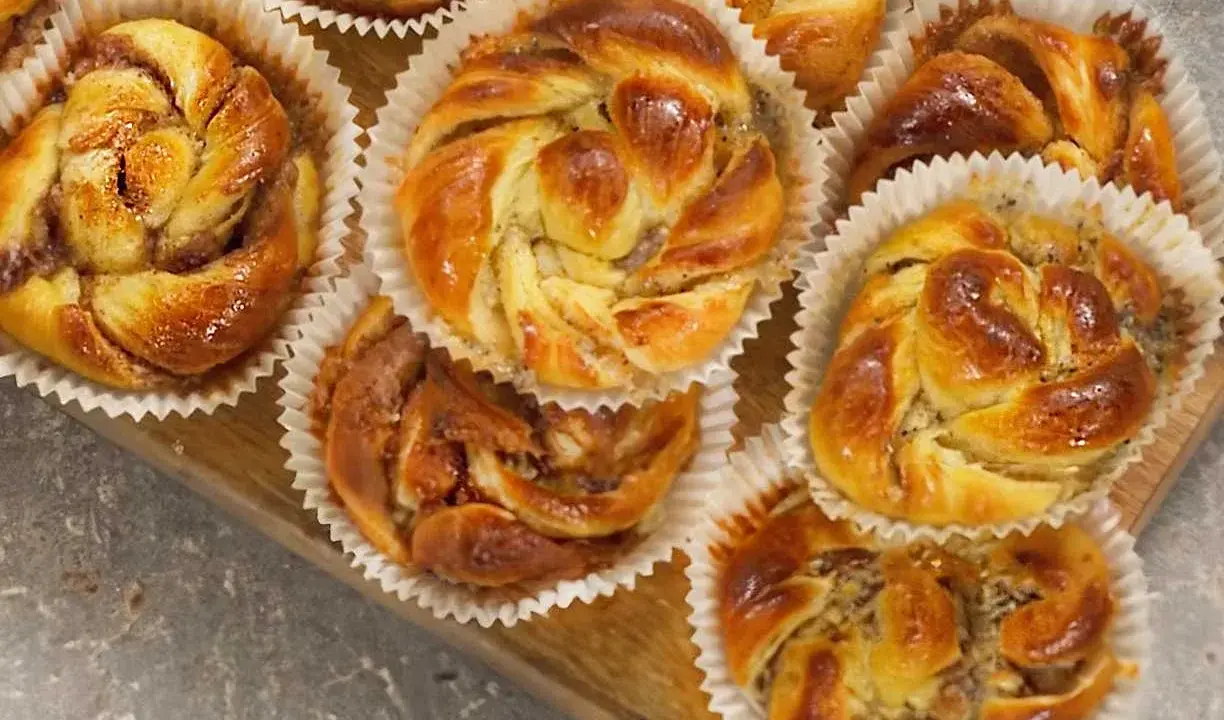 Nybakade bullar med mandelmassa, kanel och vallmofrön i pappersformar på en träbricka.