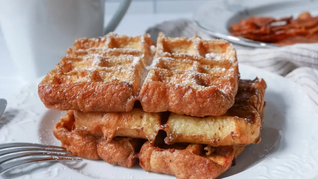 En stapel gyllene franska våfflor, pudrade med florsocker, väntar på att avnjutas. En härlig frukost eller fika.