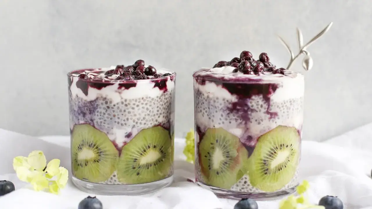 Två glas med chia pudding recept, fyllda med kiwi, yoghurt och blåbär. En vacker och hälsosam frukost.