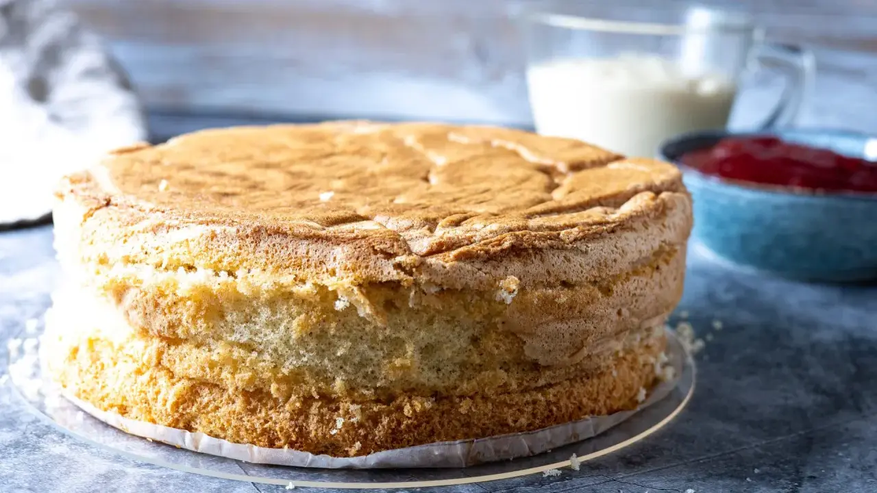 En fluffig tårtbotten, redo för fyllning. Perfekt för ditt tårtbotten recept. Bredvid syns grädde och sylt.