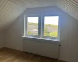 Vitt snedtak med panel och ett fönster med utsikt över träd. Gardiner saknas, men ett element finns under fönstret.