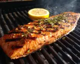 En saftig laxfilé med örter och citron ligger på grillen. Det ryker gott från den perfekta grilla laxen.
