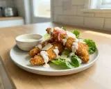 Krispiga bitar av panerad kyckling serveras på salladsbädd med krämig dressing och parmesan.