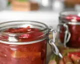 Två glasburkar med rabarberkompott, perfekt för ett gott rabarber recept. Färska rabarberstjälkar syns i förgrunden.