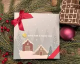 En julklapp med ett vinterlandskap och texten "GIFTS FOR A HAPPY DAY", omgiven av granris och röda bär.
