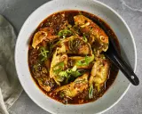 En skål med dumplings i en kryddig sås, toppad med salladslök och sesamfrön. Ett perfekt recept middag för en smakrik kväll.