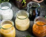 Fem små glasburkar med olika dressing till sallad: krämig vit, gul, ljusbrun, mörk och en med frön.