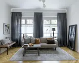 Mörka gardiner ger insynsskydd och skapar en mysig atmosfär i vardagsrummet. En bekväm soffa och en rustik soffbordsmöbel bidrar till rummets charm.
