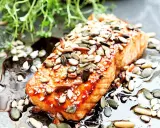 En saftig bit teriyaki lax toppad med frön, serverad i en glansig sås med gröna örter.