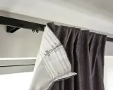 Mörka gardiner hänger på en svart gardinskena. De har en dold fåll med band och krokar, redo att fästas i gardin knoppar.
