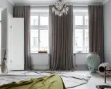 Sovrum med ljusa mörkläggningsgardiner som ramar in fönstren. En takkrona i kristall hänger ovanför.