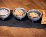 Tre skålar med kall mat, troligen dippsåser eller röror, serveras med rostat bröd på en svart stenplatta.