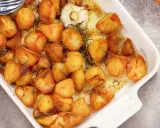 Ugnsrostad potatis i en vit form, gyllene och krispiga, med en hel vitlöksklyfta och rosmarin.