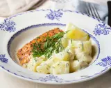 En bit stekt lax med citron och en generös portion krämig dillstuvad potatis, serverad på en vacker blåvit tallrik.