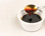 En sked häller mörk, glansig teriyakisås i en vit skål. Perfekt för ditt teriyakisås recept.