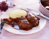 Kåldolmar recept: två kåldolmar med potatismos och lingonsylt, serverade på en tallrik med en gaffel och kniv.
