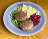 Två köttbullar med potatismos, gröna ärtor och rårörda lingon. En klassisk tallrik med svensk husmanskost.