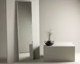 En lång, smal spegel ger spegel inspiration till ett minimalistiskt rum. En svart vas med en gren står på en vit kub.