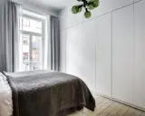 Sovrum med en stor, vit garderob med draperi. En säng med mörkt överkast står framför ett fönster med ljusgrå gardiner.