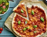 En härlig hemmagjord pizza med tomatsås och ost, toppad med färsk basilika. Bredvid en fräsch sallad med gröna bönor och tomater.