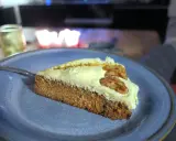 En bit saftig glutenfri morotskaka med krämig frosting och valnötter på en blå tallrik.