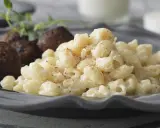 En tallrik med stuvade makaroner och köttbullar, garnerad med en kvist örter. En klassisk svensk rätt som väcker aptit.